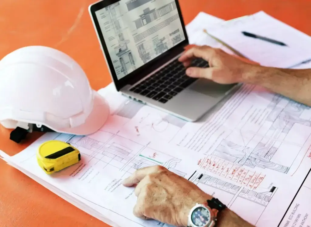 Reviewing lumber takeoff services with plans and laptop on a construction site.