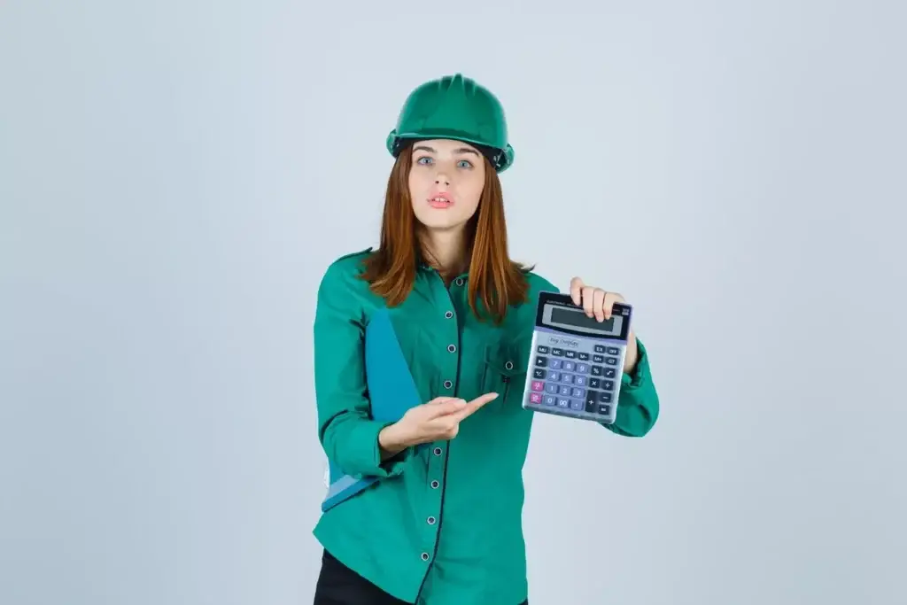 Female construction professional wearing a green hard hat and shirt, holding a large calculator and pointing at it, symbolizing budget optimization and accurate cost estimation in construction.