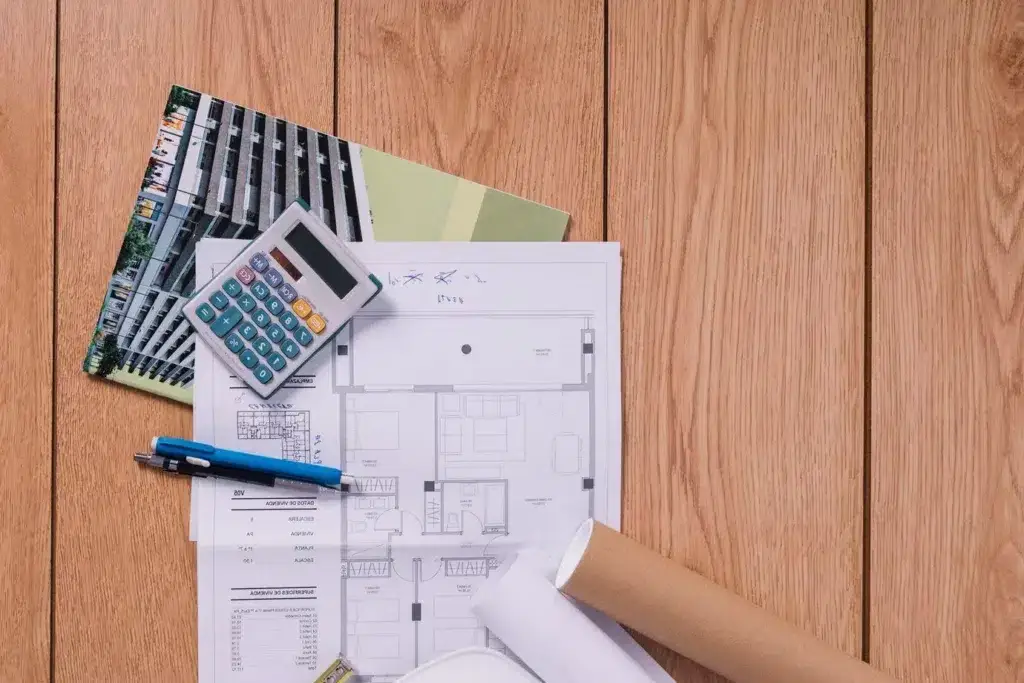 Construction cost estimate documents with blueprints, calculator, and pens on a wooden surface.