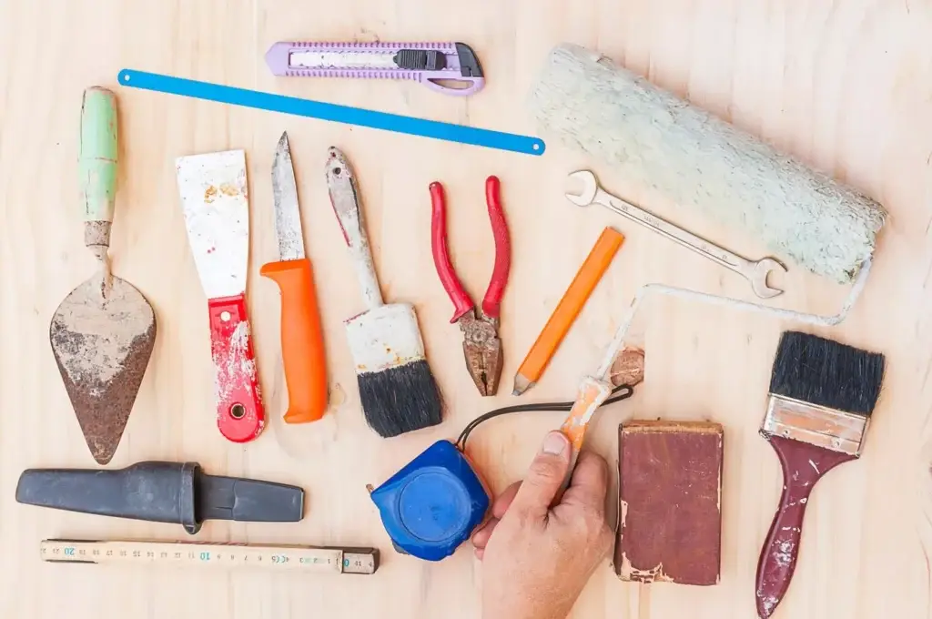 Various construction tools including brushes, pliers, knives, and measuring tape on a wooden surface.