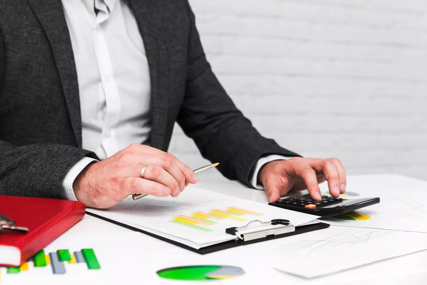 Businessman calculating labor costs with charts, graphs, and a calculator on desk.